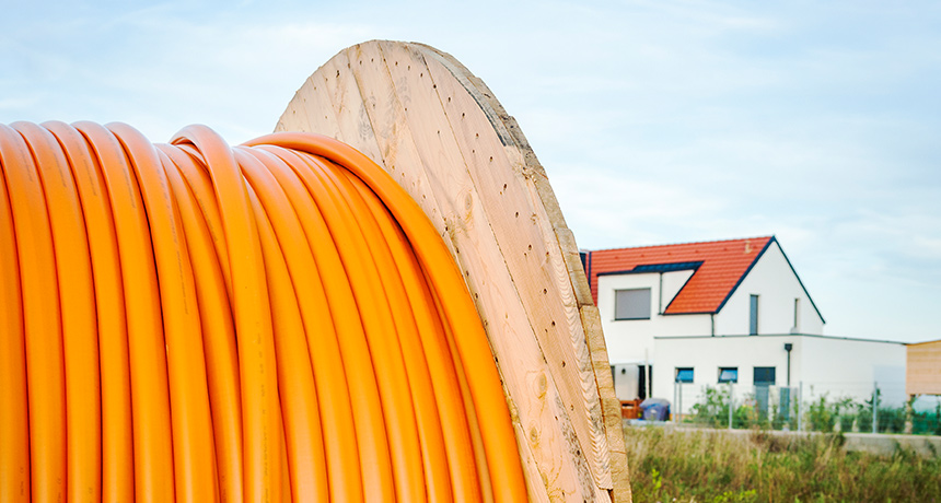A roll of orange broadband cable in front of a rural building.