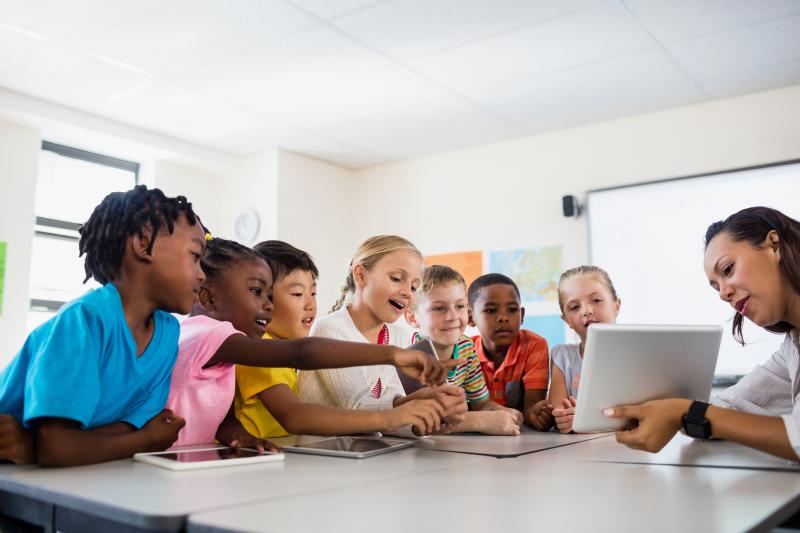 Students gathered around a teacher holding a tablet.
